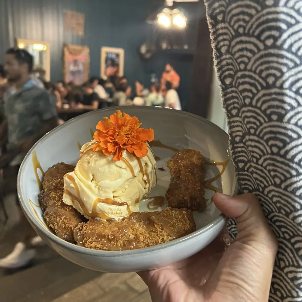 Fried apple bananas à la mode drizzled with caramel, topped with a marigold.
