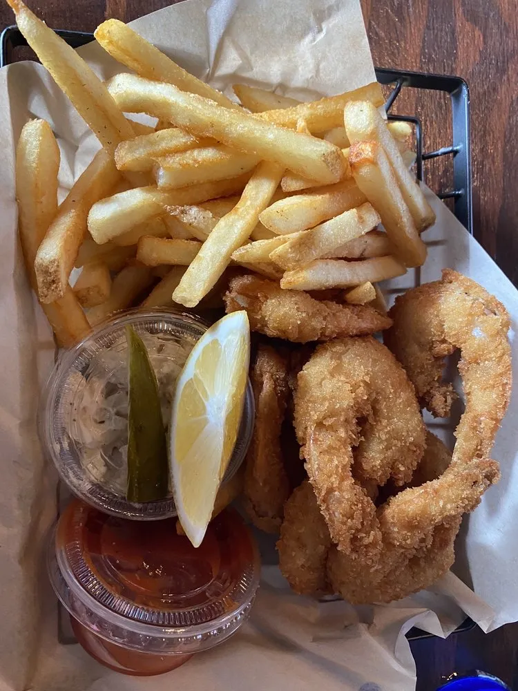 A basket of panko-fried shrimp with fries, lemon and dipping sauces.